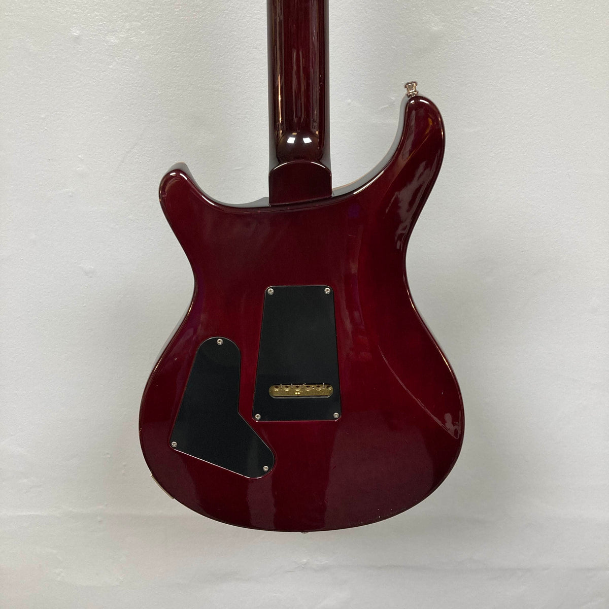 The back of a red PRS Custom 24 Angry Larry 2011 electric guitar by PRS, featuring two black plastic cover plates and a visible neck joint, shown against a plain white wall.