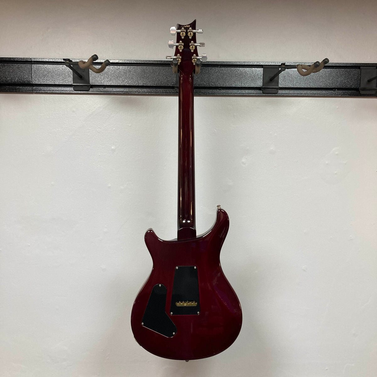 A PRS Custom 24 Angry Larry 2011 electric guitar by PRS hangs on a wall mount, displayed from the back to showcase its dark glossy finish and black plastic backplates.