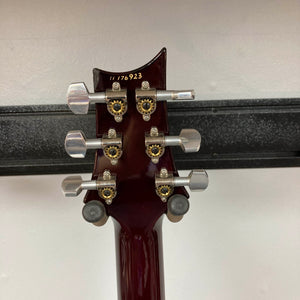 Close-up of the back of a PRS Custom 24 Angry Larry 2011 electric guitar headstock by PRS, showing six tuning pegs, serial number 176923, and part of a black wall-mounted rack.