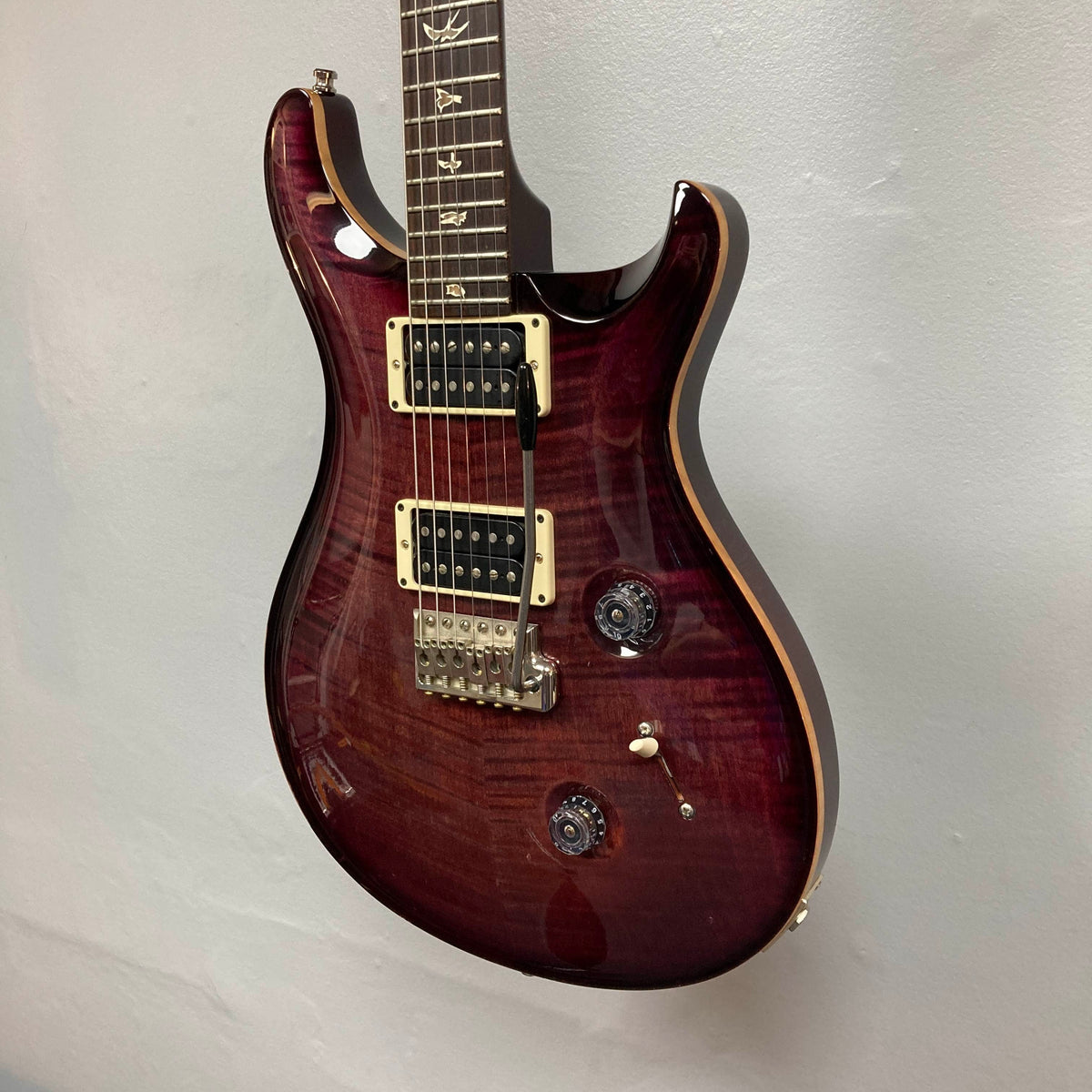 A PRS Custom 24 Angry Larry 2011 electric guitar in a rich maroon finish, featuring signature bird inlays on the fretboard and sleek humbuckers, hangs against a plain light gray wall.