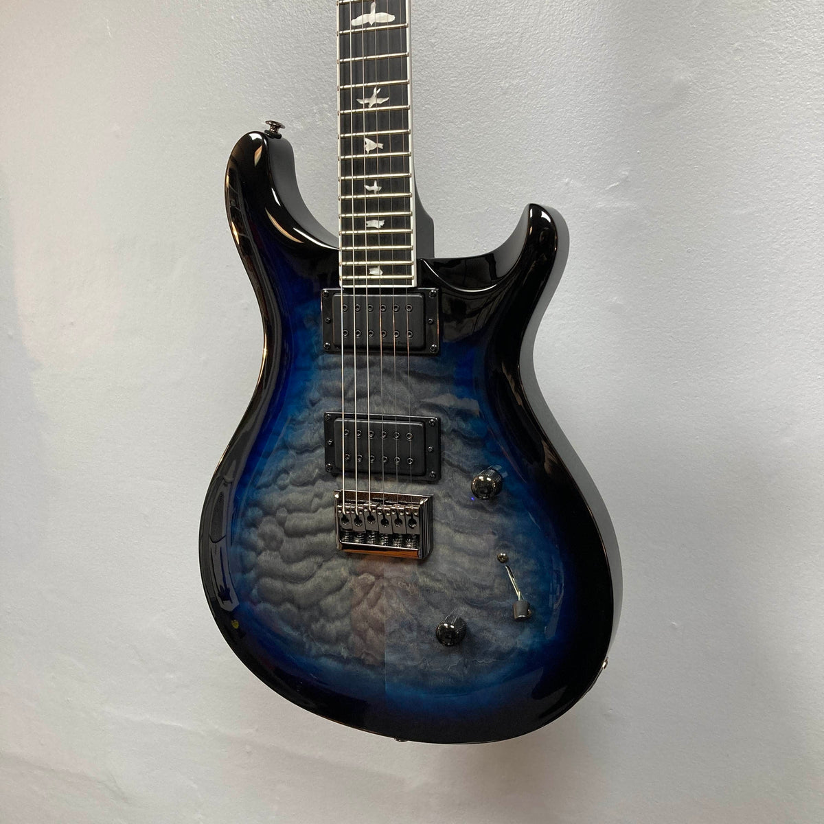 PRS SE Mark Holcomb - Holcomb Blue Burst w/Gigbag Used Consign by PRS, featuring quilted maple top, Seymour Duncan humbuckers, three knobs, and bird inlays, displayed against a white wall.