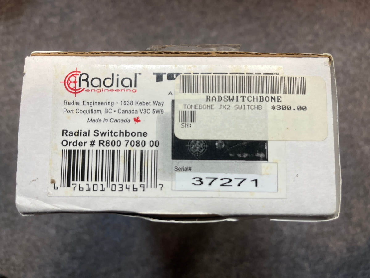 A white box labeled "Radial Tonebone Switchbone JX-2 AB-Y Class-A Switcher (Preowned)" by Radial Engineering, with a $300 price tag, plus order and serial numbers and company address.
