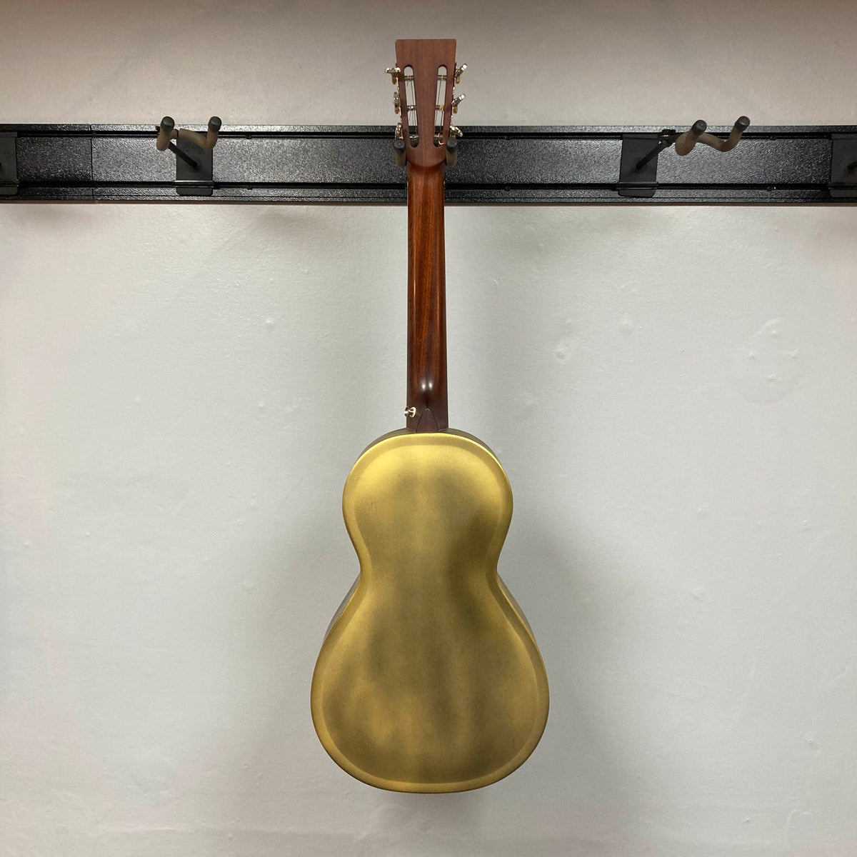 Back view of the Republic Parlor Resolian Antique Bronze Resonator w/Case by Republic, featuring a single cone design, displayed on a wall-mounted black guitar rack against a white wall.