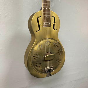The Republic Parlor Resolian Antique Bronze Resonator w/Case by Republic, featuring a metallic body with f-shaped sound holes and a single cone, is mounted vertically against a plain light gray wall.