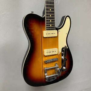 A Reverend Greg Koch Signature Gristle 90 electric guitar in 3-Tone Burst with a white pickguard, two cream-colored Fishman Gristle 90 pickups, Bigsby tremolo, and chrome hardware is shown against a plain gray wall. Brand: Reverend.