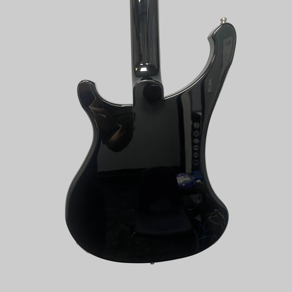 Mounted on a white wall, the sleek black Rickenbacker 4003 Bass Guitar – 2020 Jetglo w/Case reflects a person and objects in the room. Its lustrous finish and signature curves capture the timeless allure of this iconic Rickenbacker bass.