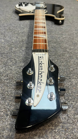 Close-up of a near-mint Rickenbacker 620 in Jetglo, focusing on the branded headstock as it rests on gray carpet; includes original case.