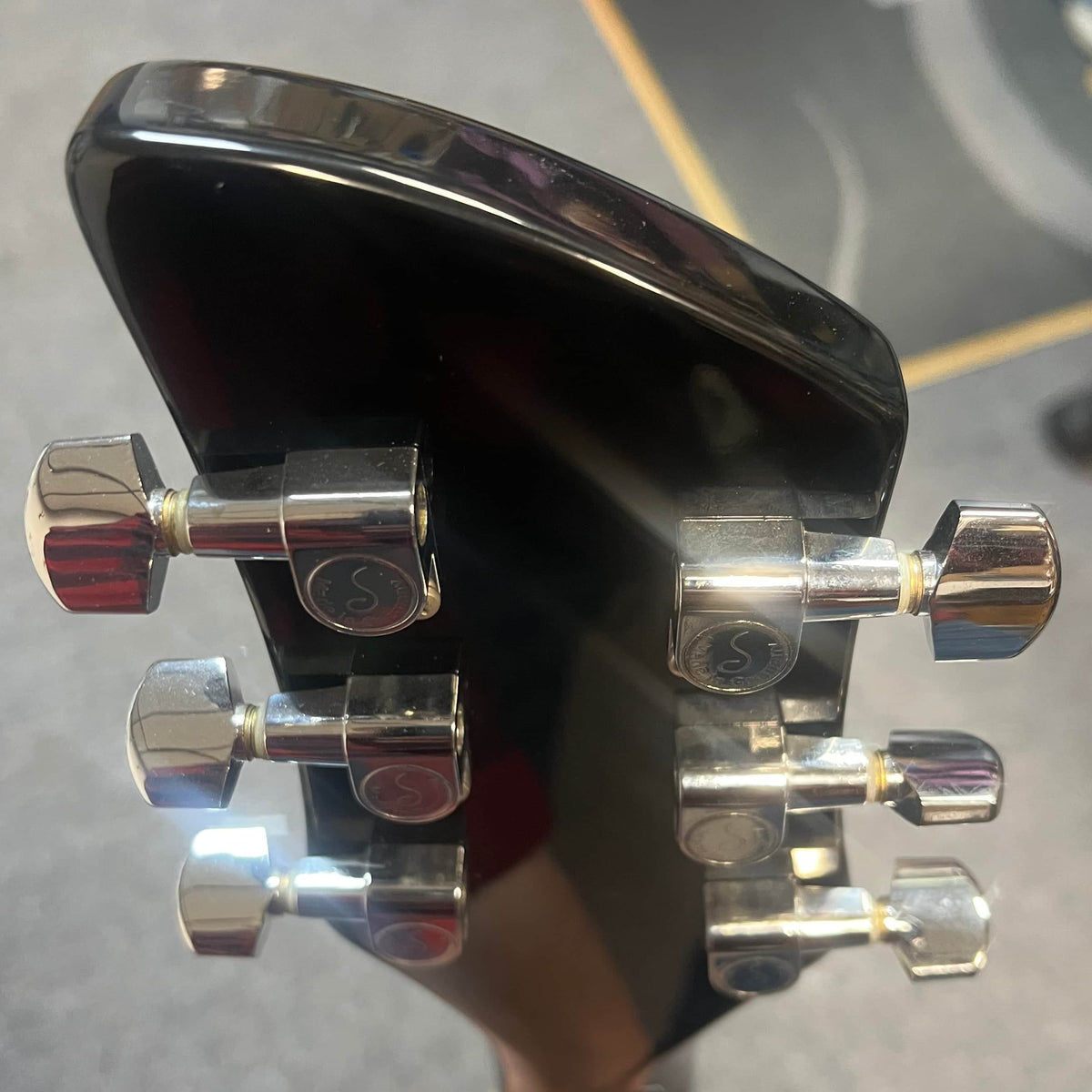 Close-up of the back of a near-mint Rickenbacker 620 – Jetglo headstock, featuring six chrome tuning pegs with "S" details. The background is blurred. Includes original case.