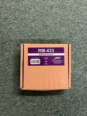 A brown cardboard box labeled "RTI RM-433 433MHz RF Receiver Module" by Remote Technologies Inc (RTI) sits on gray carpet. The label shows a barcode and "Made in Taiwan"—designed for easy integration with RTI control systems.