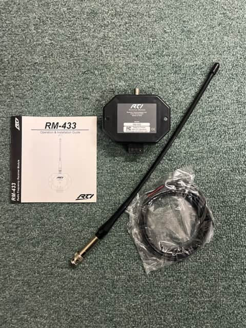 A Remote Technologies Inc (RTI) RM-433 433MHz RF Receiver Module, antenna, coiled cable in plastic, and operation manual for RTI control systems are shown on a green carpeted surface.
