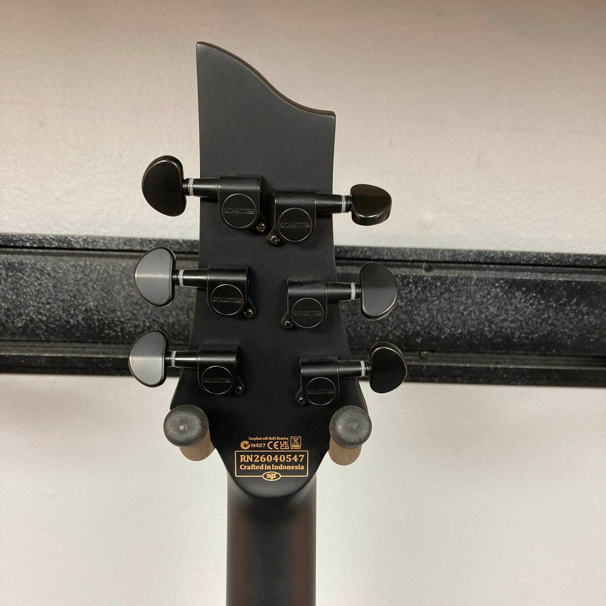 Back of a Schecter C-1 Hydro-Dip Purple Obsidian headstock featuring six black tuning pegs and a plate displaying serial number RN26045047 and “Crafted in Indonesia.”