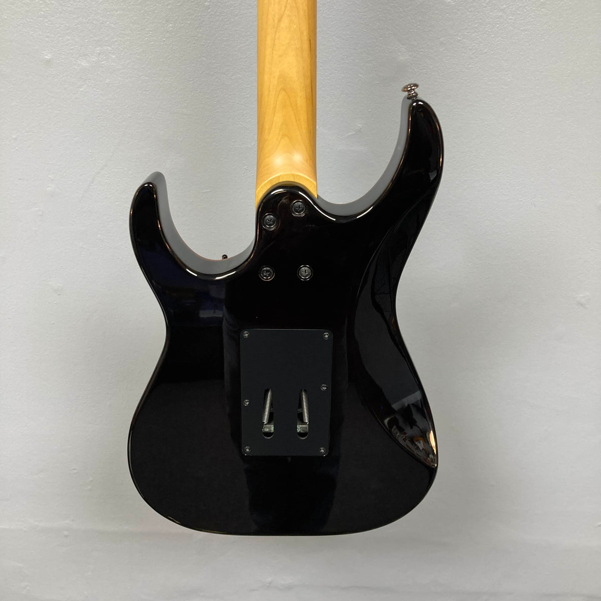 Rear view of a Schecter Extreme Banshee 6 FR CHARCOAL BURST electric guitar with case, featuring a natural wood neck, set against a plain light-colored wall.
