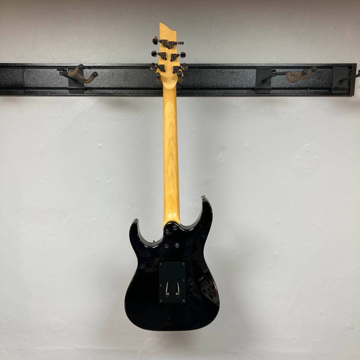 A Schecter Extreme Banshee 6 FR CHARCOAL BURST Electric Guitar w/case by Schecter hangs on a wall rack, shown from the back with the neck up and body down—sleek and high-output, featuring a Floyd Rose bridge system.