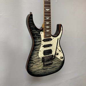 Schecter Extreme Banshee 6 FR CHARCOAL BURST Electric Guitar w/case, featuring a quilted maple top, three pickups, pearloid pickguard, and double-cutaway body, hangs on a light-colored wall.