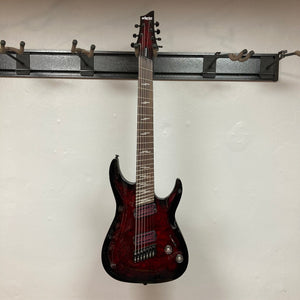 Schecter Omen Elite-7 Multiscale electric guitar on a hook, highlighting close-up details of the finish blemishes and humbucker pickups.