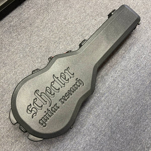 A Schecter Solo-II Custom Trans Black Burst with case, branded "Schecter," lies on a gray carpeted floor. The case is hard, black, and embossed with "Schecter guitar research," made to fit the Solo-II Custom model.