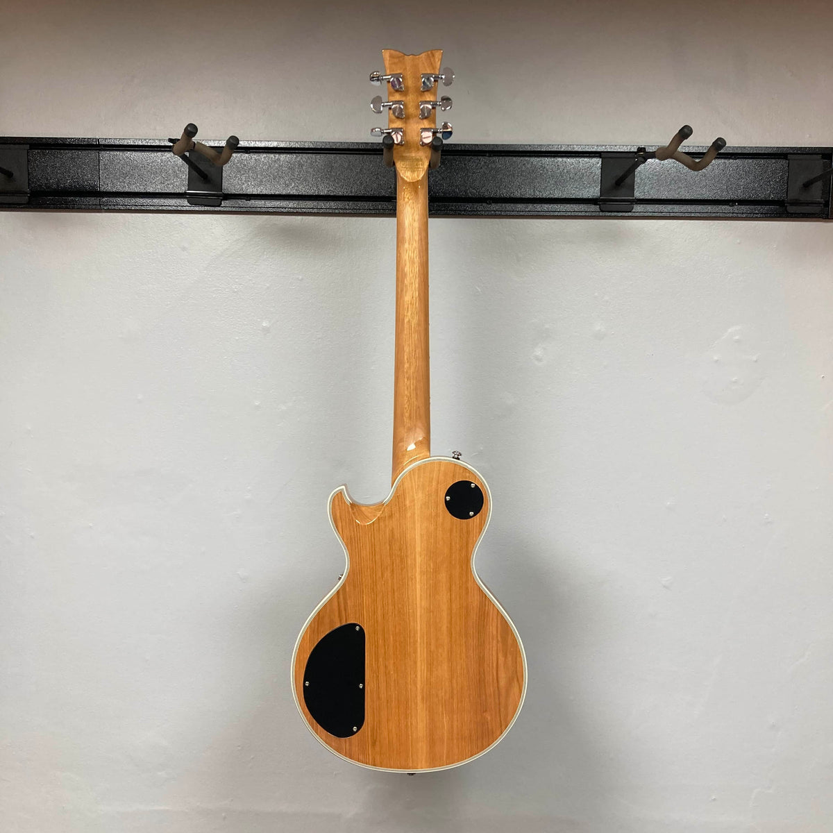 A Schecter Solo-II Custom Trans Black Burst w/Case Used electric guitar by Schecter hangs on a wall-mounted rack, shown from the back with its control cavity covers visible.