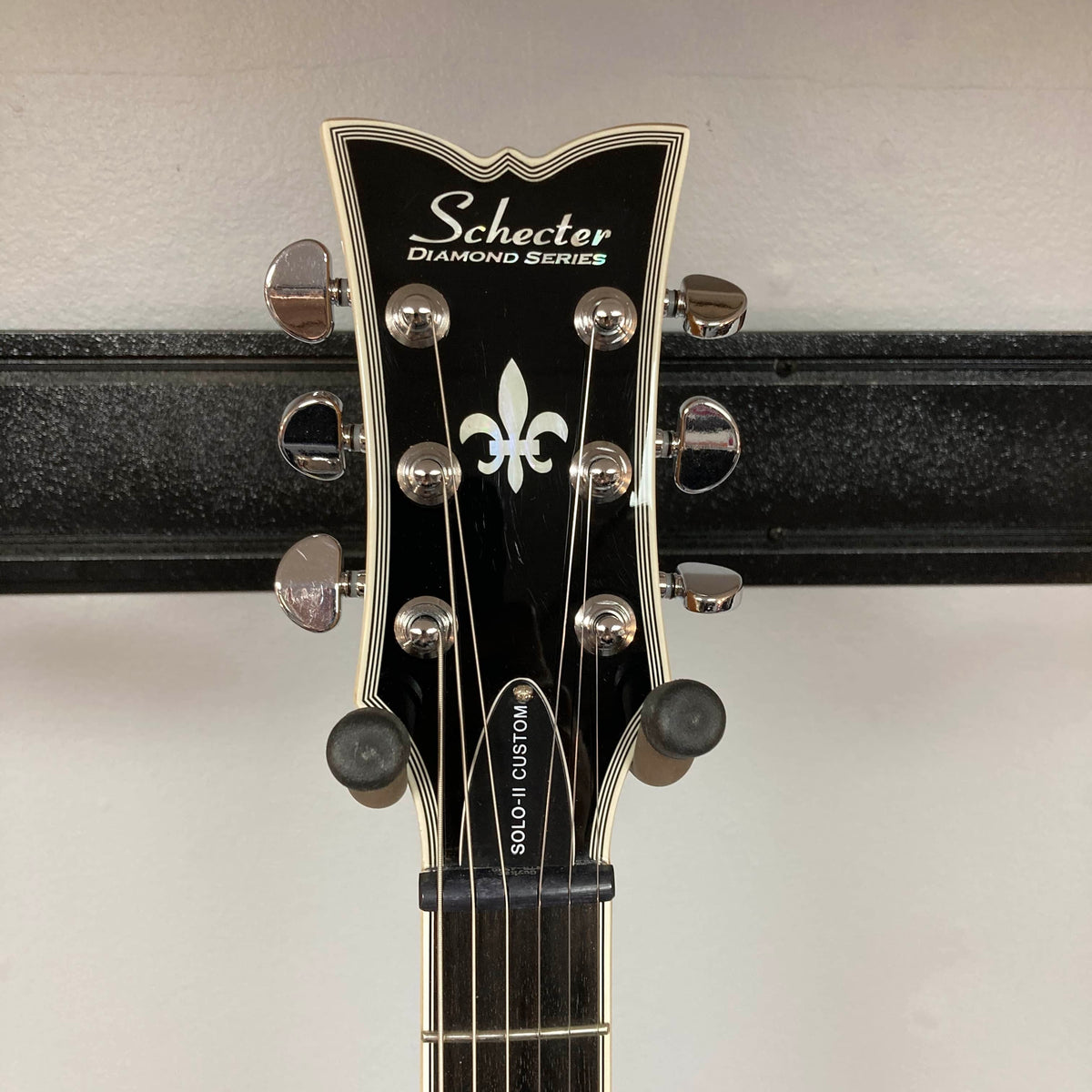 Close-up of a Schecter Solo-II Custom Trans Black Burst headstock with tuning pegs and fleur-de-lis inlay—featuring premium Schecter USA Pasadena pickups.