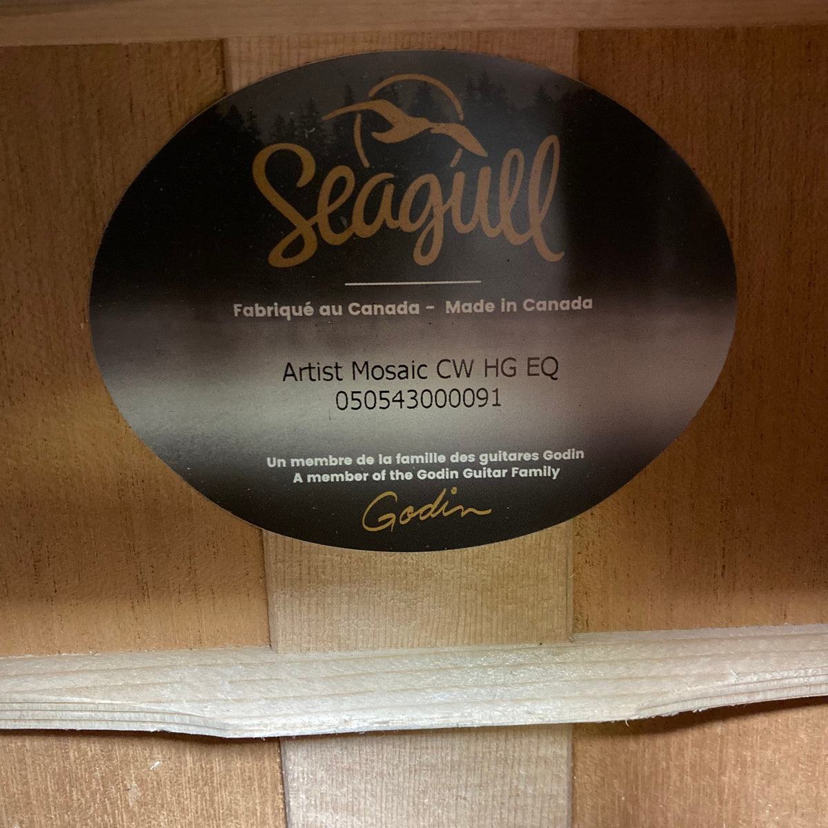 Seagull Artist Mosaic CW HG EQ guitar with black and gold label on a wood surface.