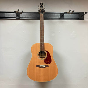 A Seagull S6 QI Slim Acoustic Guitar w/Hard Case (USED/consign) hangs on a wall-mounted rack against a plain white background, available now for consignment sale.