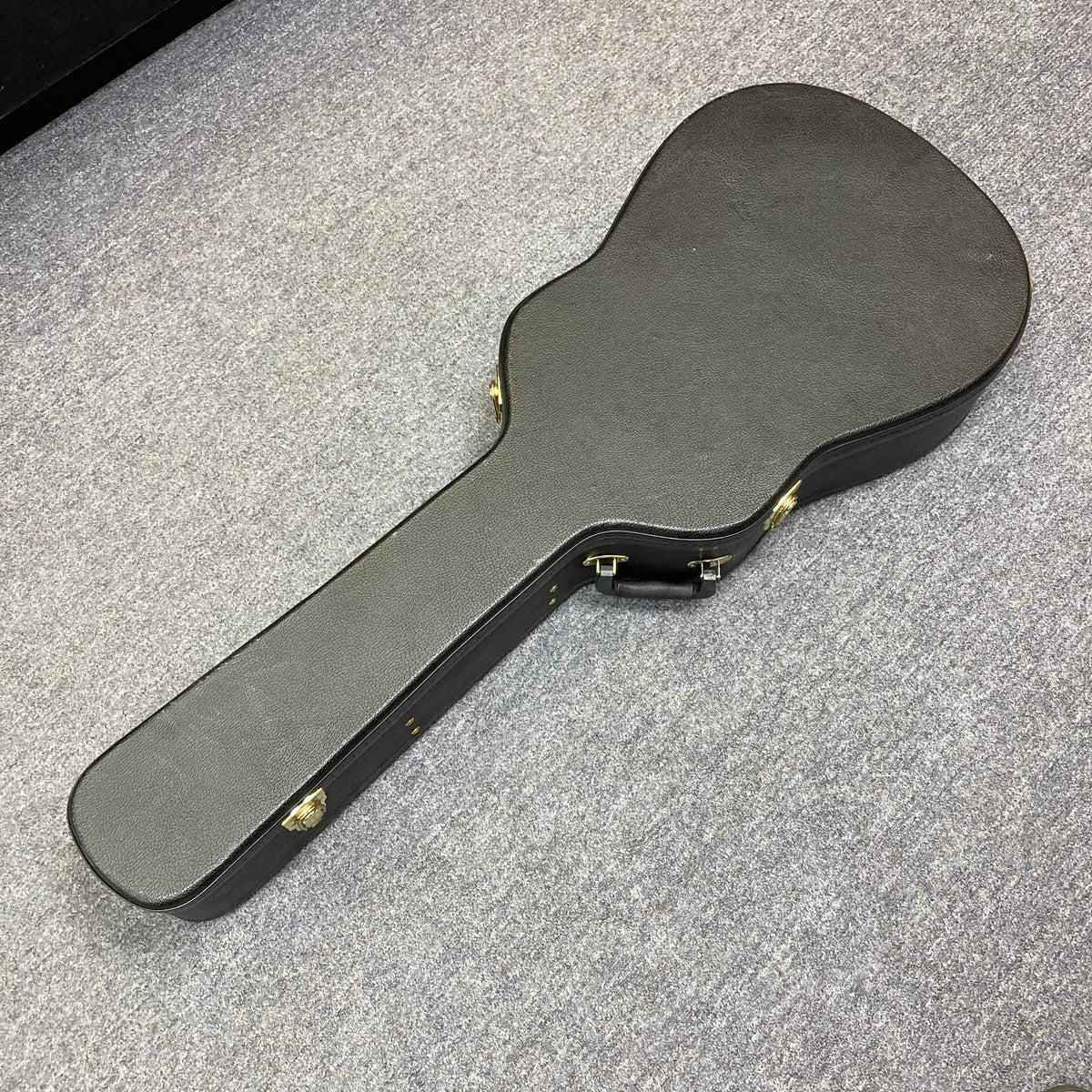 A black Seagull S6 QI Slim Acoustic Guitar with a solid spruce top sits in its hard case with gold latches on a light gray carpet, ready for travel and protection. Used/consign.
