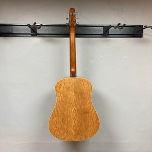 A Seagull S6 QI Slim Acoustic Guitar w/Hard Case - USED/consign hangs by its neck on a black wall-mounted rack, seen from the back against a plain light-colored wall.