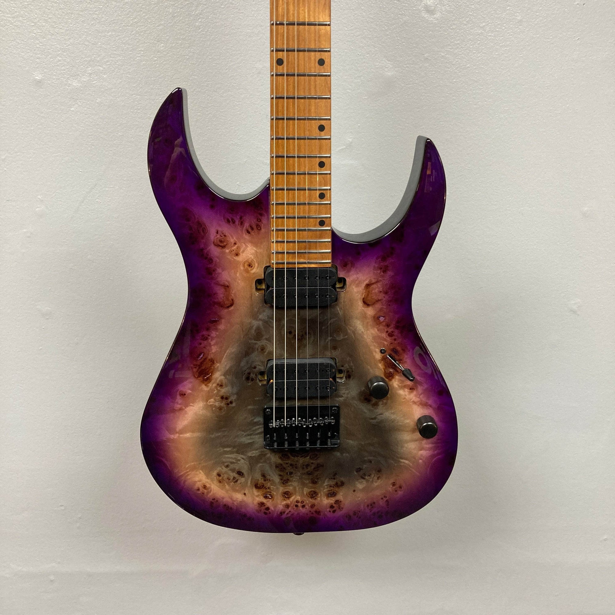 The Spira S-450 Trans Purple TPP electric guitar by Spira features a natural wood and purple burst finish, a modern D profile neck, double-cutaway body, two Villain humbuckers, tremolo bridge, and black knobs, shown against a white wall.