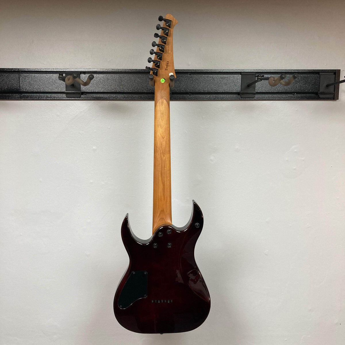 Spira S-457 TPP Trans Purple Burst Electric Guitar showcasing its back, highlighting the solid-body, seven-string design, and tuning machines on a light wall-mounted display.