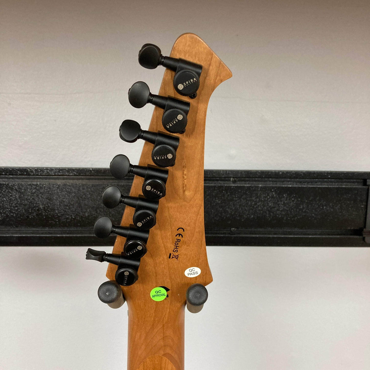 Spira S-457 TPP Trans Purple Burst Electric Guitar headstock with black Spira tuning machines, QC, and compliance stickers, showcasing quality craftsmanship and precision tuning stability.