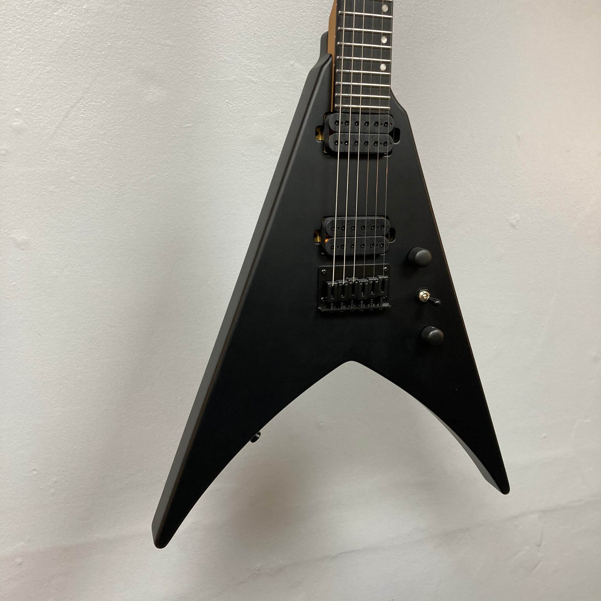 A Spira V-400 MBK electric guitar by Spira, featuring a black V-shaped body, high-output humbuckers, three control knobs, and a three-way switch, photographed against a plain white wall.
