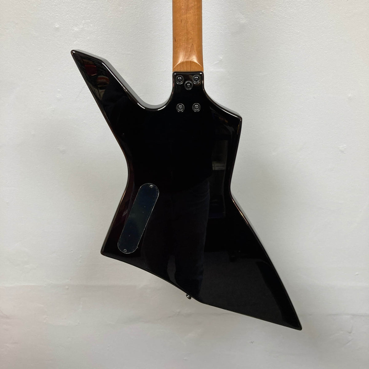 Back view of the Spira X-500 TBK E by Spira, a black metal guitar with a distinctive angular body shape, fast neck, and visible back plate, set against a plain white wall.