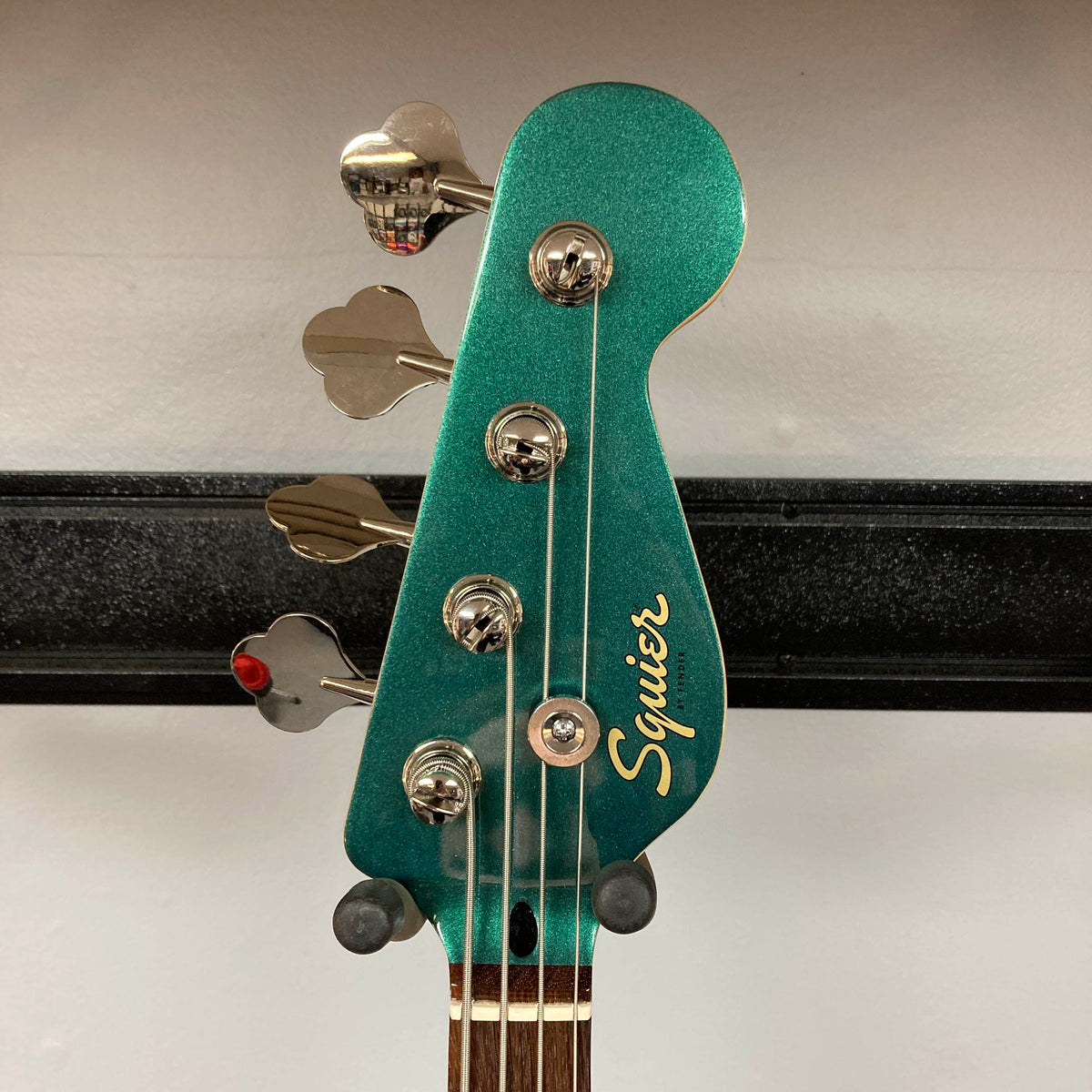 A close-up of the Sherwood Green Squier Paranormal Rascal Bass HH Refurb headstock, featuring four tuning pegs and the gold Squier logo.