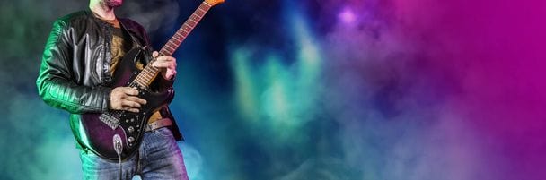 Man performing on a foggy stage playing a purple guitar. 
