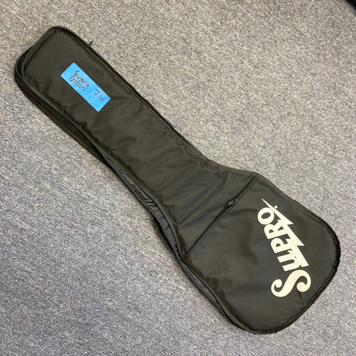 A black Supro soft-sided gig bag rests on a gray carpet, featuring a blue label marked "2352 me case" near the top. Ideal for storing your Supro 1296 Silverwood British Racing Green w/Gigbag Used guitar with Gold Foil pickups.