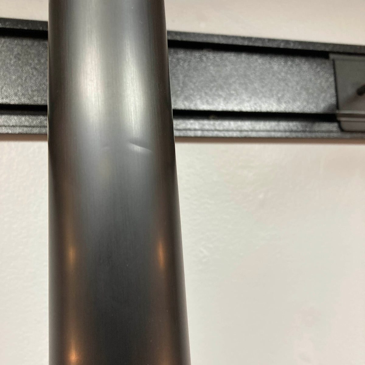 Close-up of a metallic cylindrical pole with a small dent, positioned in front of a wall-mounted black rail, next to a Supro 1296 Silverwood guitar in British Racing Green equipped with Gold Foil pickups (used), by Supro.