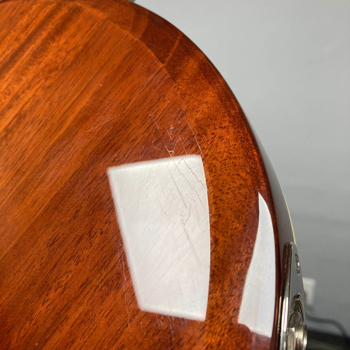 A close-up of the polished wooden body of a Supro 1296 Silverwood British Racing Green w/Gigbag (Used) showcases subtle scratches and a reflected light source on its sleek surface. This image emphasizes the refined finish and suggests unique features like Gold Foil pickups, characteristic of Supro craftsmanship.