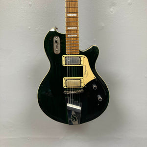 A striking Supro 1296 Silverwood electric guitar in British Racing Green, featuring two Gold Foil pickups, a tremolo bridge, and gold hardware, is mounted against a plain gray wall.