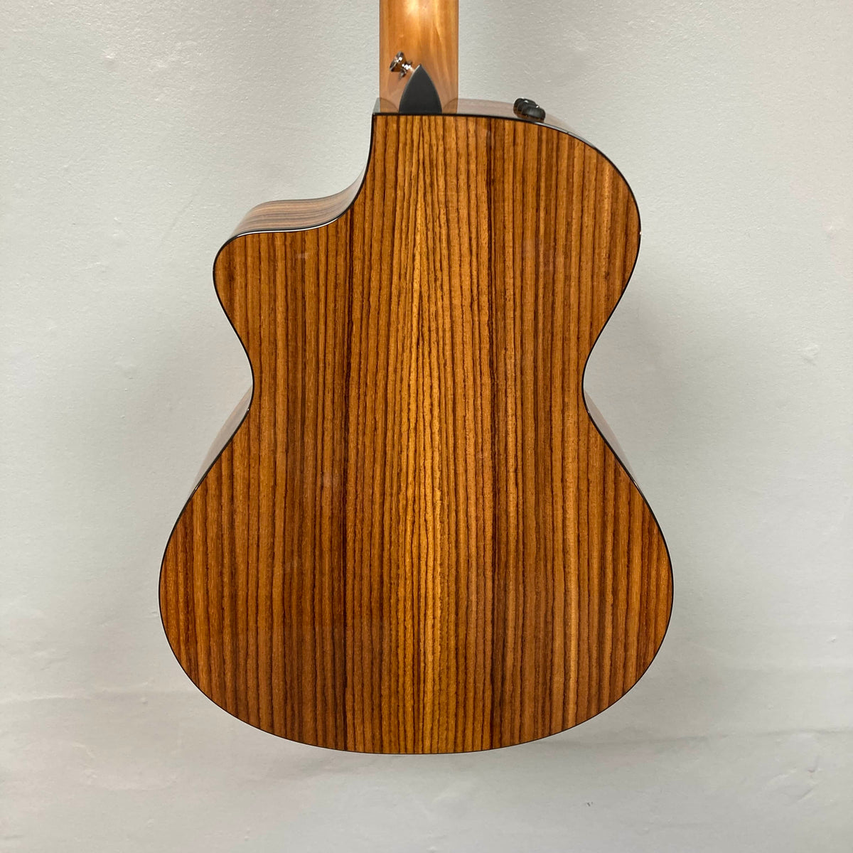 A close-up of the Taylor 212ce Plus w/Gigbag Used Consign highlights its natural wood grain back and elegant cutaway design.