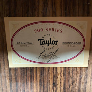 Taylor 212ce Plus w/Gigbag Used Consign label features the model name and signature, highlighting Taylor’s renowned craftsmanship on a wooden surface—quality from the makers of iconic acoustic guitars.
