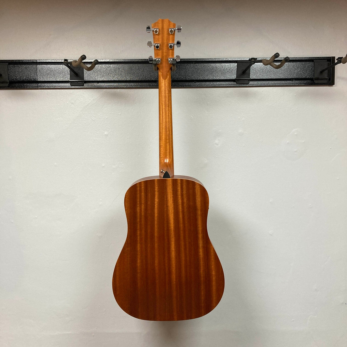 Back view of a Taylor Academy 10e Acoustic-Electric Guitar w/GigBag Used hanging by its headstock on a wall mount.