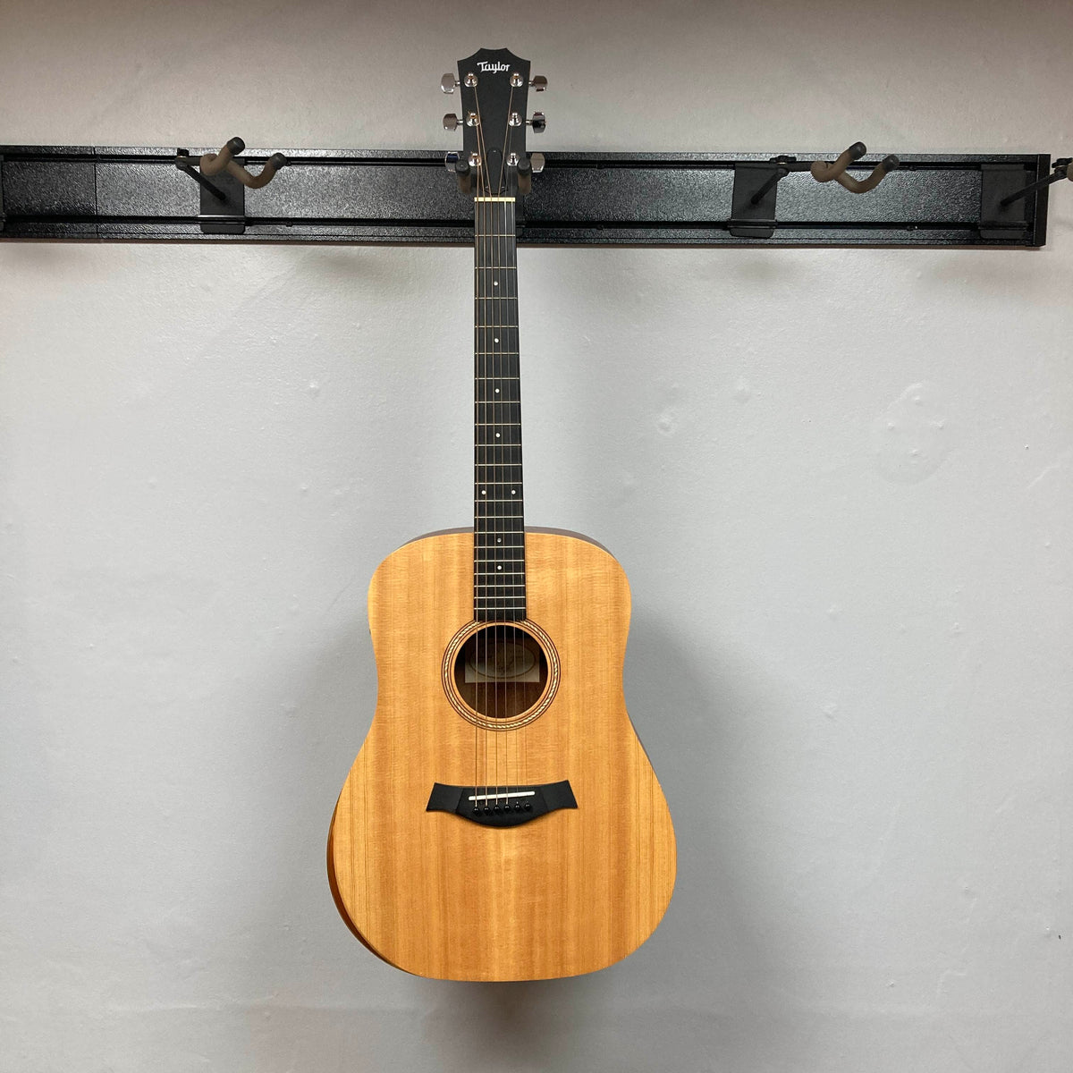Taylor Academy 10e Acoustic-Electric Guitar w/GigBag Used hanging on a wall-mounted display rack.