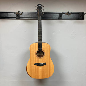 Taylor Academy 10e Acoustic-Electric Guitar w/GigBag Used hanging on a wall-mounted display rack.