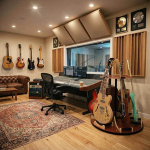 A recording studio featuring guitars on the Carousel™ Deluxe Rotating Guitar Stand by A&S Crafted Products and on the floor, a mixing console, computer monitors, soundproof panels, a rug, and awards on the wall.