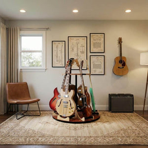 A home music room featuring A&S Crafted Products' The Carousel™ Deluxe Rotating Guitar Stand | Combined Unit for multiple guitars, an amp, a wall-mounted guitar, framed art, a brown chair, rug, and floor lamp.
