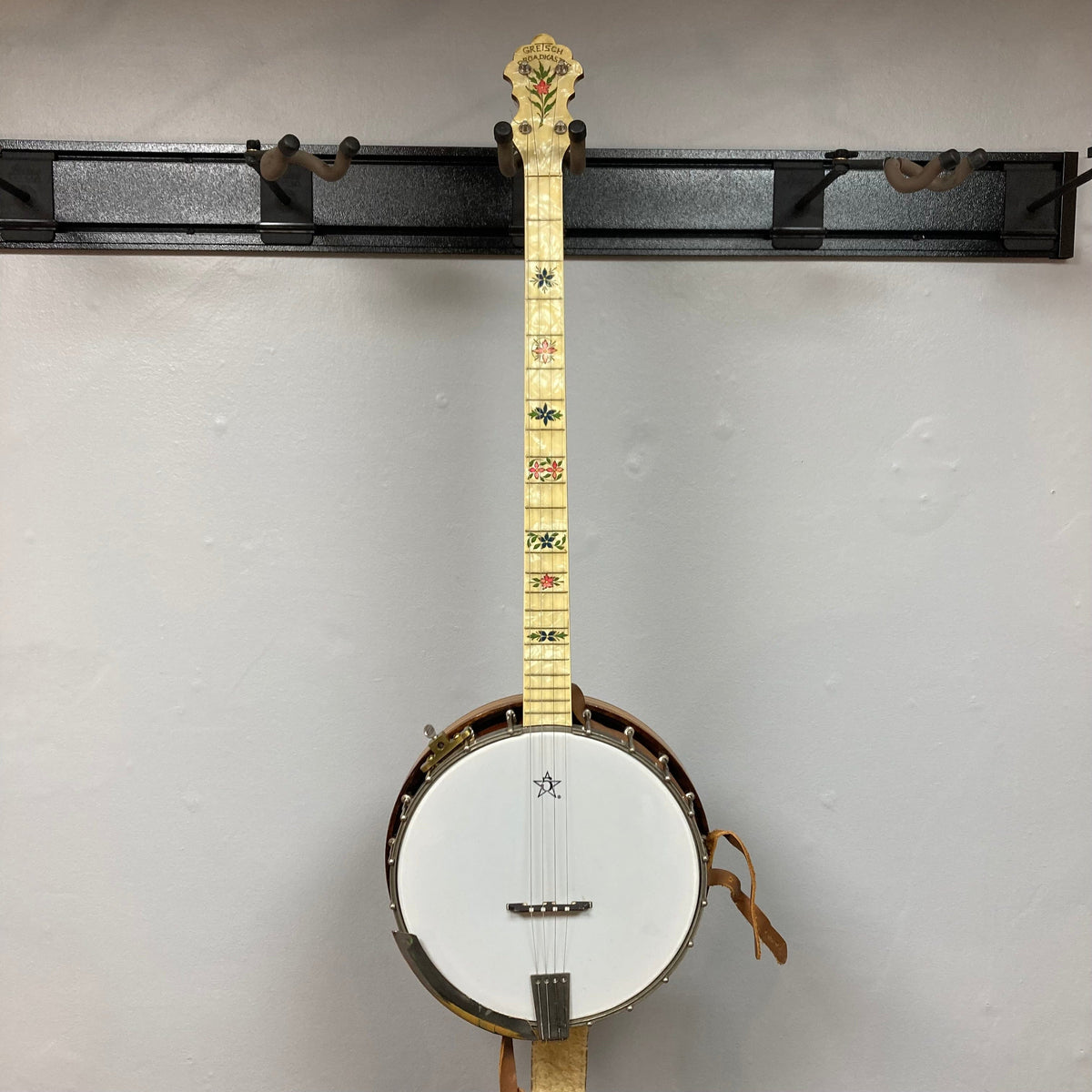 Vintage 1920-1930s Gretsch Broadkaster 4-String Tenor Banjo displayed on a wall, showcasing its maple body, floral inlay headstock, and nickel-plated hardware.