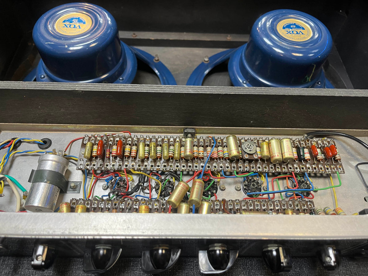 Close-up of the internal circuitry and components of a vintage 1963 Vox AC30/6 Normal amplifier, showing resistors, capacitors, wiring, Woden transformers, and two blue VOX speakers; includes original JMI egg footswitch and flight case.