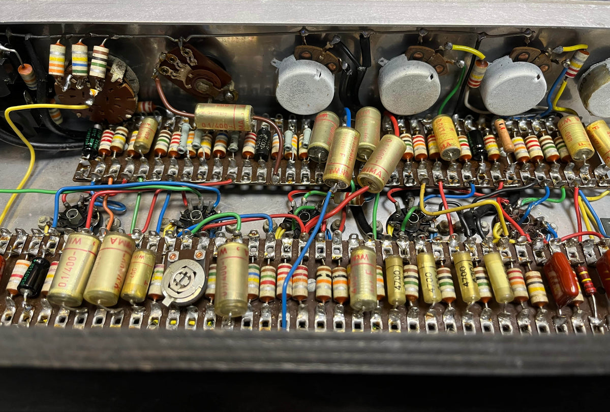 Close-up of a vintage circuit board with resistors, capacitors, wires, and potentiometers, featuring classic Woden transformers from the 1963 Vox AC30/6 Normal by Vox, including original JMI egg footswitch and flight case.
