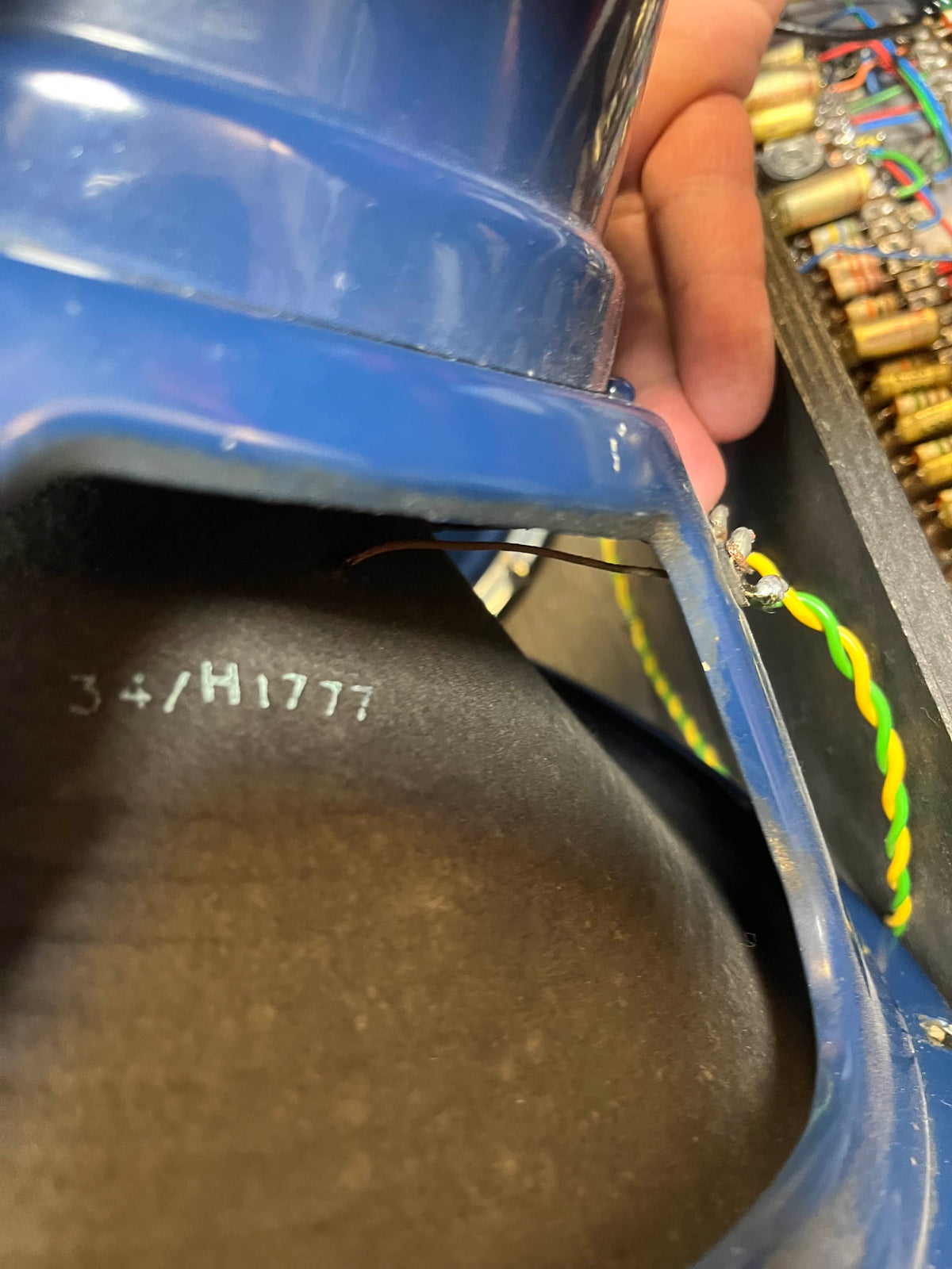 Close-up of a blue speaker frame—likely Celestion Blue T530—with code "34/H1777" and green-yellow wires, set against electronics from a Vintage 1963 Vox AC30/6 Normal amp by Vox, plus its original JMI egg footswitch and flight case.