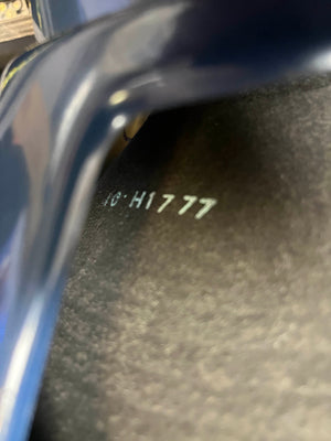 Close-up of a dark metallic surface stamped with "HC H1777," partially covered by a curved object—likely part of a Vintage 1963 Vox AC30/6 Normal amplifier by Vox, shown with its original JMI egg footswitch and flight case.