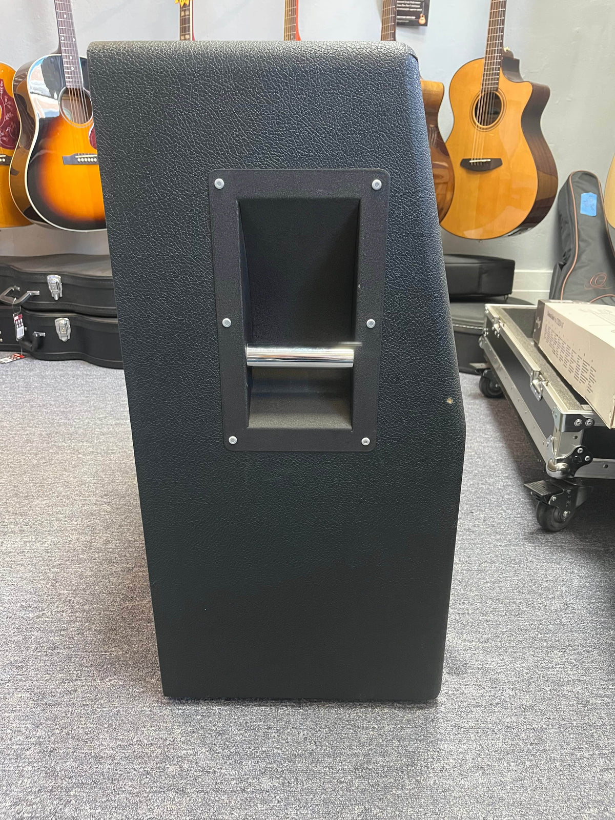 A 1969 Marshall 4x12 Cabinet with matching Celestion T1281 Greenbacks is shown in black with a metal side handle, surrounded by acoustic guitars hanging on the wall in the background.